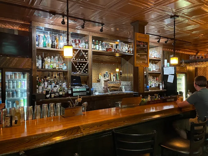 O'Pub's main bar — pressed-tin ceiling, hanging pendants, bottles lined deep along a wood back-bar.