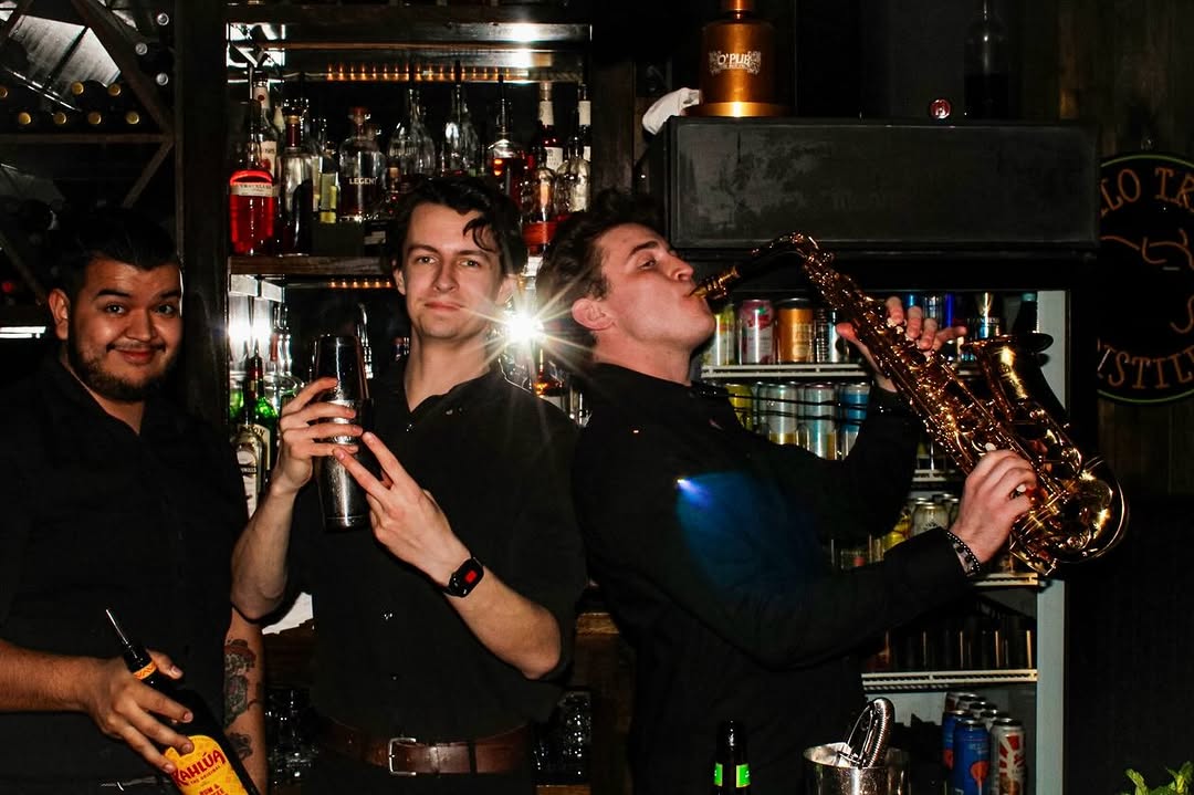 A trio behind the O'Pub bar — bottles backlit, a saxophone in play.
